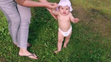 Şapkalı güzel kız annesinin yardımıyla ilk adımlarını dışarıda atıyor.