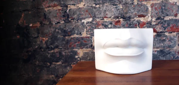 White plaster lips of antique statue standing on wooden surface against old brick wall