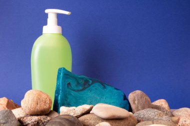 Arkadaki çakıl taşının ve tuvalet kağıdının üzerinde duran ince, mavi naneli el yapımı sabun parçası.