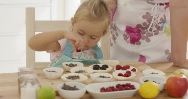 Маленькая девочка кладет ягоды на кексы — стоковое видео