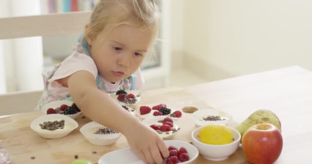Girl putting berries on muffins on table — Stock Video