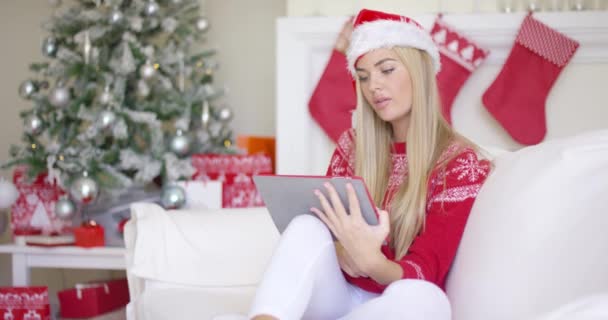 Mujer joven rubia bonita sentada en el sofá con touchpad — Vídeos de Stock