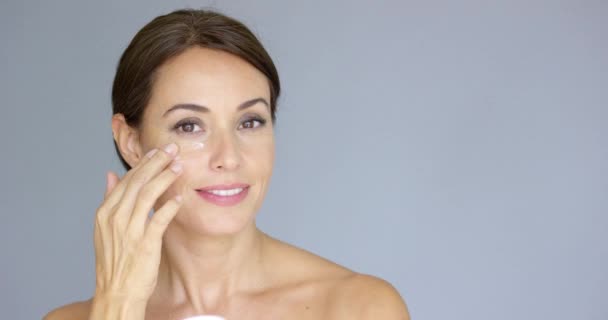 Hermosa mujer joven aplicando crema facial — Vídeos de Stock