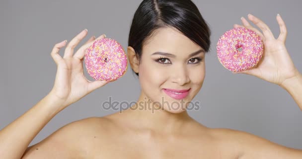 Mujer sonriente sosteniendo dos rosquillas a sus ojos — Vídeos de Stock