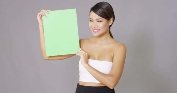 Mujer sosteniendo una tarjeta en blanco sobre fondo gris — Vídeo de stock