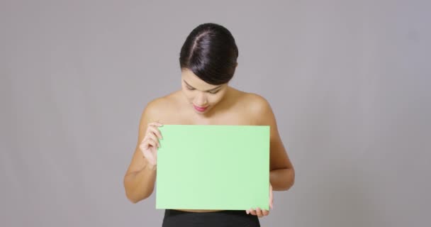 Mujer sosteniendo una tarjeta en blanco sobre fondo gris — Vídeo de stock