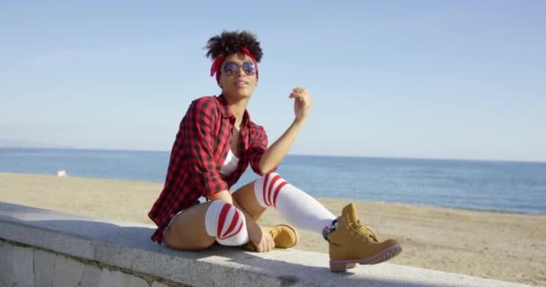 Trendy jonge vrouw ontspannen op een strand muur — Stockvideo