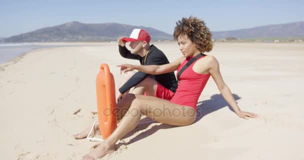 Mannelijke en vrouwelijke badmeesters zittend op strand — Stockvideo