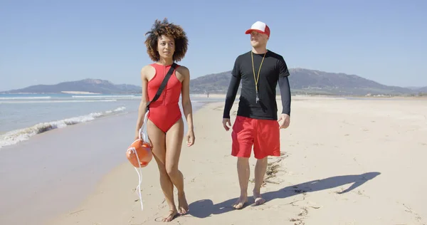 Vrouwelijke en mannelijke badmeesters wandelen langs strand — Stockfoto