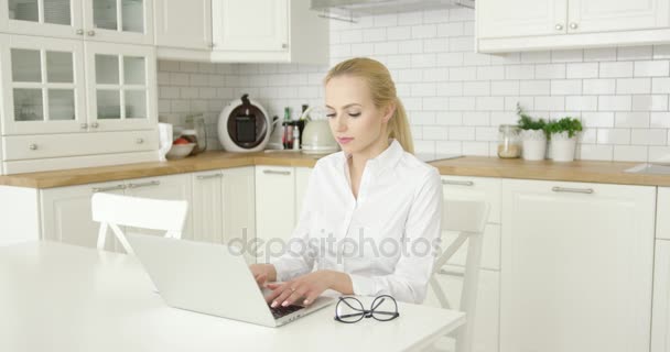 Mujer joven usando el ordenador portátil en la cocina — Vídeos de Stock