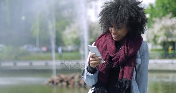 Chica sonriente con teléfono en la fuente — Vídeo de stock