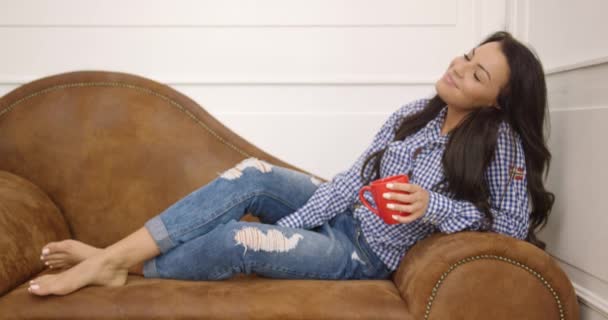 Молода жінка з чашкою на дивані — стокове відео