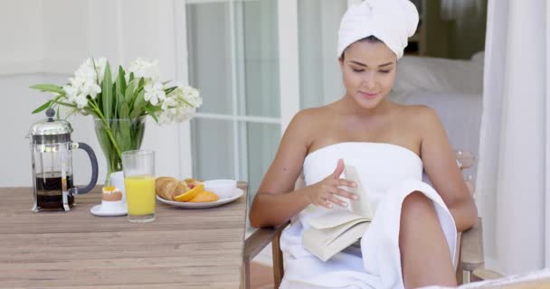 Женщина в полотенце чтение книги за столом — стоковое видео