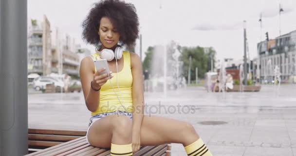 Chica deportiva utilizando el teléfono inteligente en el banco — Vídeo de stock