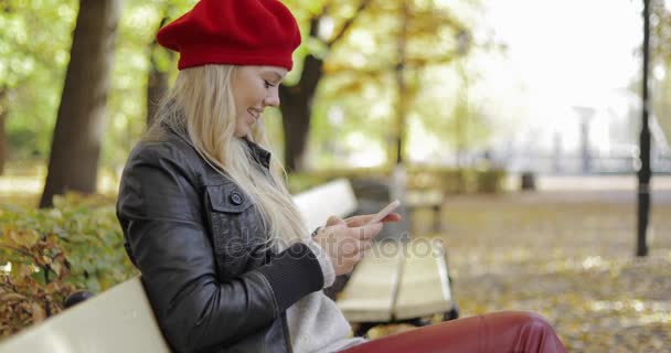 在使用智能手机的贝雷帽看起来快乐的女人 — 图库视频影像