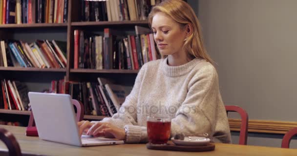 Donna in maglione utilizzando il computer portatile in biblioteca — Video Stock