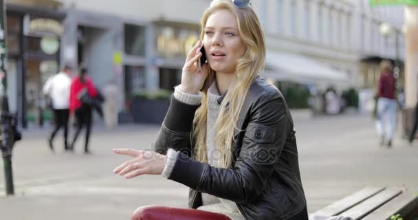 Женщина на скамейке запасных и говорит по телефону — стоковое видео