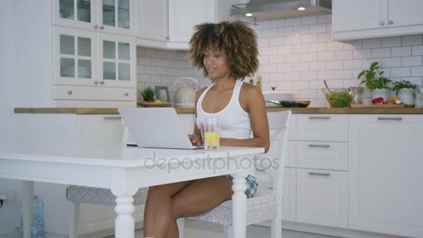 Mujer joven usando el ordenador portátil en la cocina — Vídeos de Stock