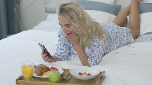 여 자가 침대에서 아침 식사 하는 동안 스마트폰 사용 하 여 — 비디오