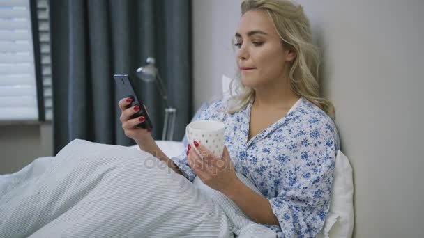 スマート フォンとマグカップのベッドの上の女性 — ストック動画
