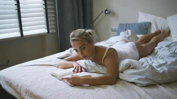 Vacker kvinna läser bok på säng — Stockvideo