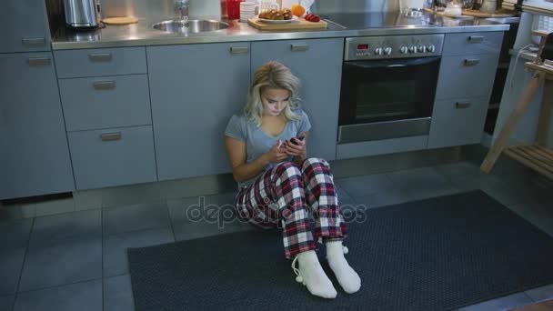 Preciosa mujer navegando teléfono inteligente en piso de cocina — Vídeos de Stock