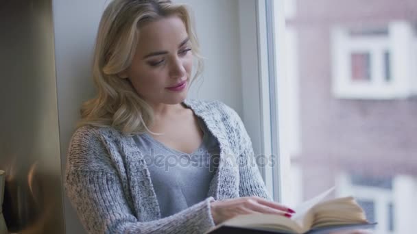 Женщина читает книгу у окна — стоковое видео