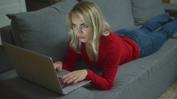 Serious woman with laptop lying on couch — Stock Video