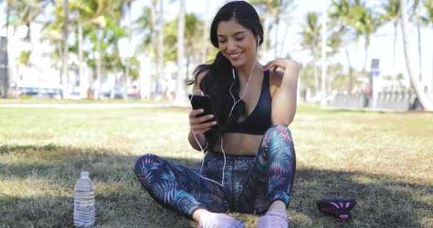 Chica bonita con teléfono en el entrenamiento en el parque — Vídeo de stock