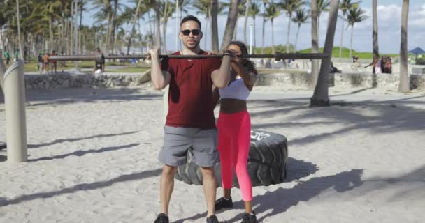 Mujer ayudando a hombre con entrenamiento en la playa — Vídeo de stock