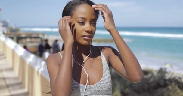 Ethnic woman in earphones and sportswear at seaside — Stock Video