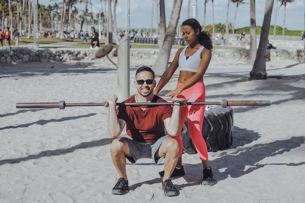 Woman helping man with workout on beach — Stock Photo, Image