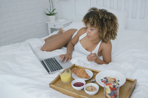 Mujer contenta usando el ordenador portátil mientras come —  Fotos de Stock