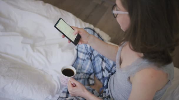 Νεαρή γυναίκα πίνοντας καφέ και χρησιμοποιώντας το smartphone — Αρχείο Βίντεο