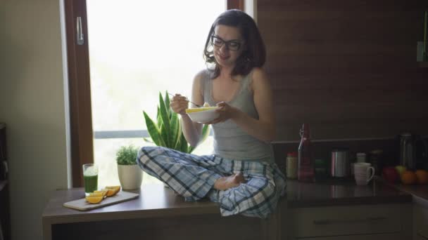 Wanita muda duduk di atas meja dan makan sarapan — Stok Video