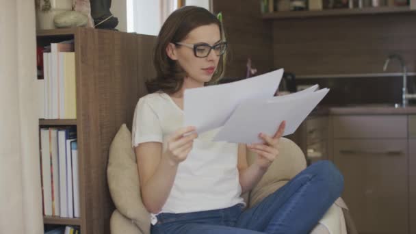 Young woman sitting in armchair reading papers — Stock Video