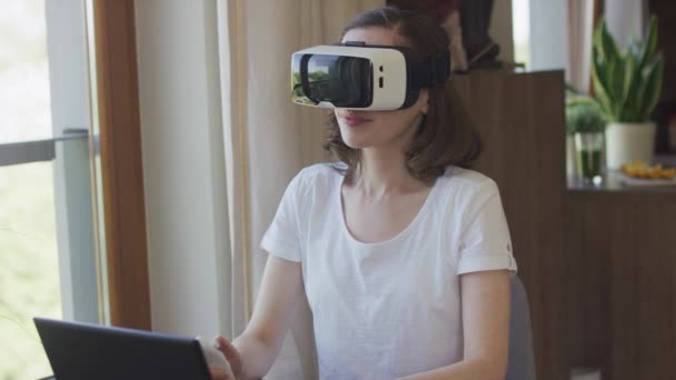 Молодая женщина сидит дома в гарнитуре VR — стоковое видео