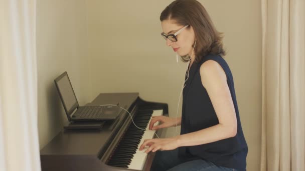 用手提电脑和耳机弹奏钢琴的微笑女人 — 图库视频影像