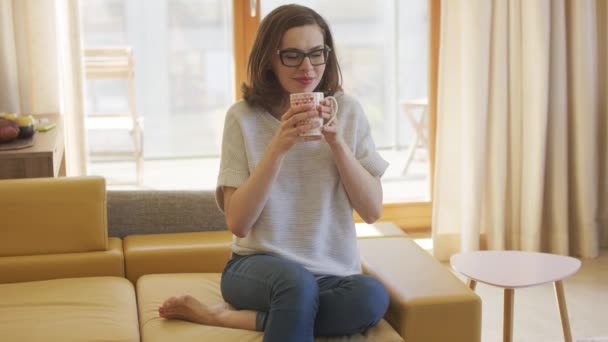 Mujer con taza sentada en el sofá — Vídeos de Stock