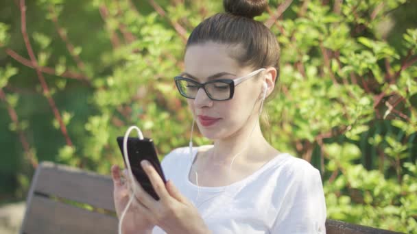 Улыбающаяся женщина в наушниках со смартфоном — стоковое видео
