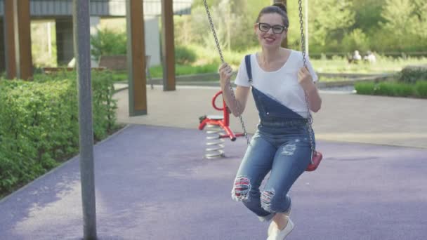 Aantrekkelijke lachende vrouw swingen op speelplaats — Stockvideo