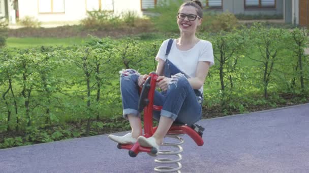 Atractiva mujer cabalgando juguete de primavera en el patio de recreo — Vídeos de Stock