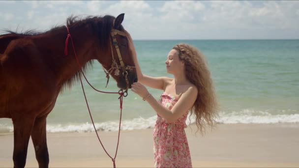 Long haired woman stroking brown horse in face on seaside — Stock Video