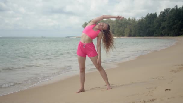 분홍색 수영복을 입은 활달 한 여자 가 해변에서 운동을 하고 있다 — 비디오