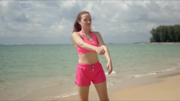 Spokojna kobieta w różowej odzieży sportowej rozciągająca szyję na plaży — Wideo stockowe