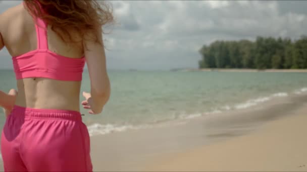 穿着粉色运动服在海滩上跑步的活跃女子 — 图库视频影像