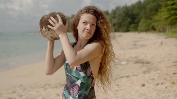 Спантеличена жінка трясе кокос на пляжі — стокове відео