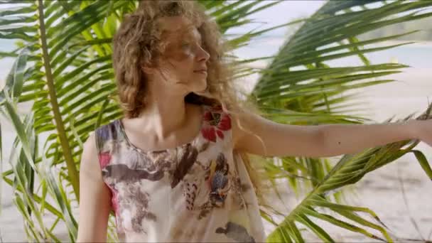 Спокойная женщина, стоящая напротив пальмовой ветки на пляже — стоковое видео