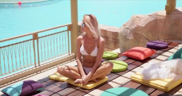 Stilvoll gebräunte Frau sitzt mit überkreuzten Beinen auf bunten Kissen auf offener Terrasse — Stockvideo