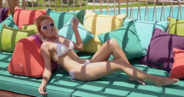Şık, neşeli kadın havuz kenarında yastıkla kanepede güneşleniyor. — Stok video